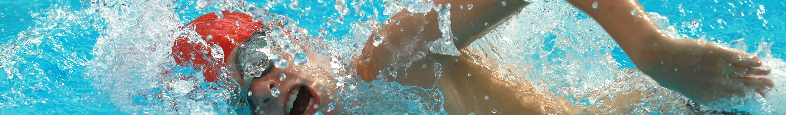 Person schwimmt im Wasser mit roter Badekappe und Schwimmbrille, Wasser spritzt um sie herum.