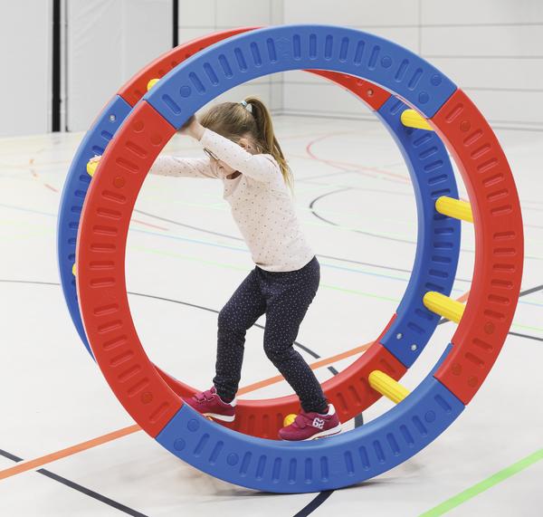 Kind balanciert in einer bunten Spielrolle in einer Sporthalle.