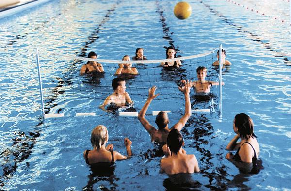 Menschen spielen Wasser-Volleyball in einem Hallenbad mit klarem blauen Wasser.