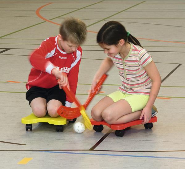 Kinder spielen in der Halle Rollhockey mit Schlägern und Ball auf Rollbrettern.