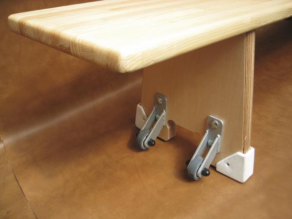 Klapptisch aus Holz mit Metallbeschlägen und Schutzkappen auf braunem Boden.