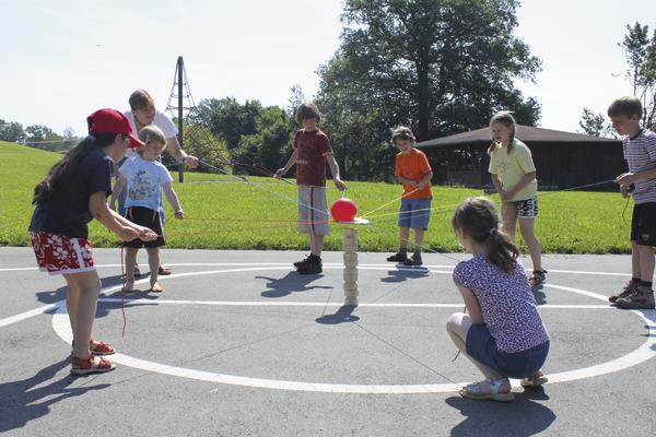 Kinder spielen im Freien ein kooperatives Ball- und Turmbau-Spiel auf dem Asphalt.