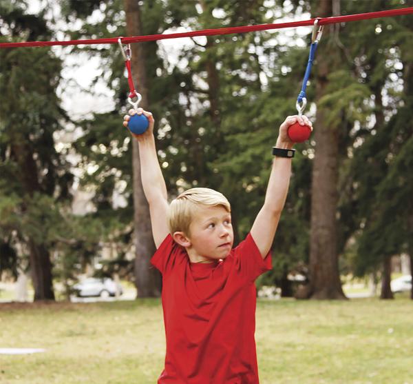 Junge in rotem Shirt hängt an Klettergriffen im Park, umgeben von Bäumen.