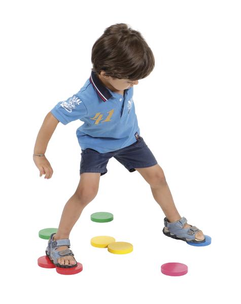 Kind spielt mit bunten Schwimmscheiben auf weißem Hintergrund, trägt blaues Shirt und Shorts.