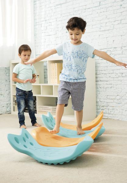 Zwei Jungen spielen drinnen auf einem bunten Balancier-Spielgerät aus Kunststoff.