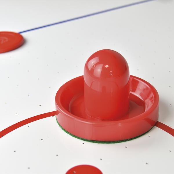Roter Schläger und Puck auf weißem Airhockey-Tisch mit roten Markierungen.