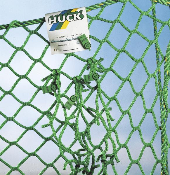 Grünes Schutznetz von Huck mit Etikett vor blauem Himmel, Nahaufnahme der Netzstruktur.