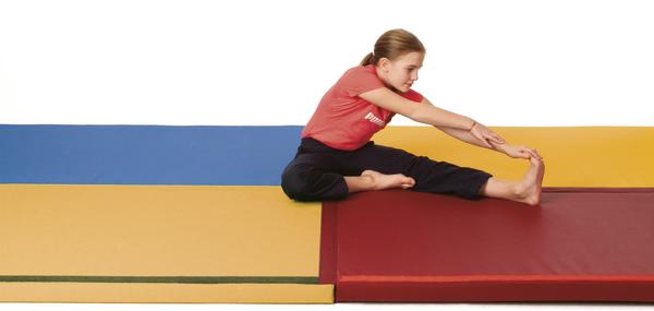 Mädchen dehnt sich sitzend auf Gymnastikmatte, trägt rotes Shirt und schwarze Hose.