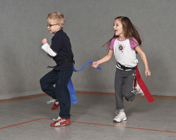 Kinder spielen Flag-Football in der Halle, Mädchen jagt Jungen mit Flaggen am Gürtel.