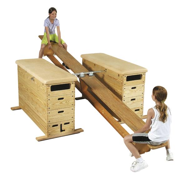 Kinderspiel auf einer Holzwippe zwischen zwei gepolsterten Turnkästen.