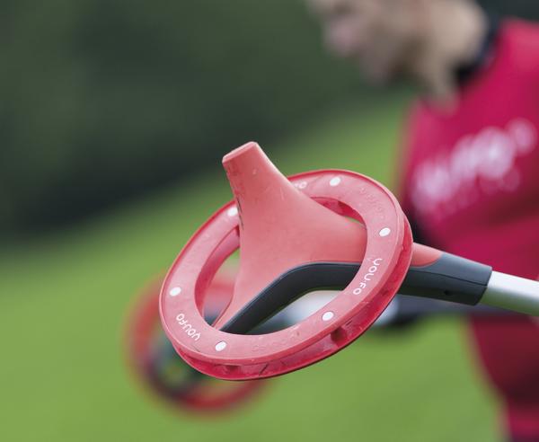 Rotes Trainingsgerät mit Griff und Ring vor unscharfem Hintergrund im Freien.