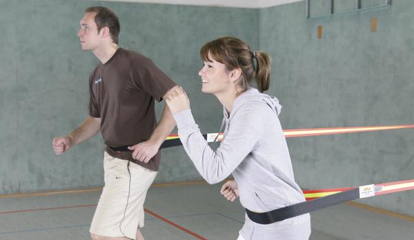 Mann und Frau trainieren mit Widerstandsbändern in der Sporthalle für Kraft und Ausdauer.