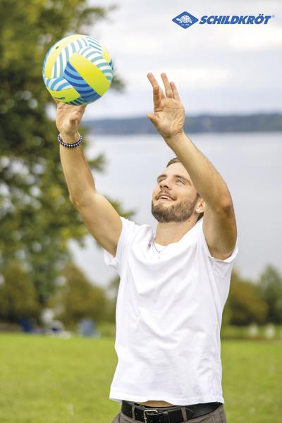 Mann spielt Volleyball im Freien mit Schildkröt Volleyball vor See und Bäumen.