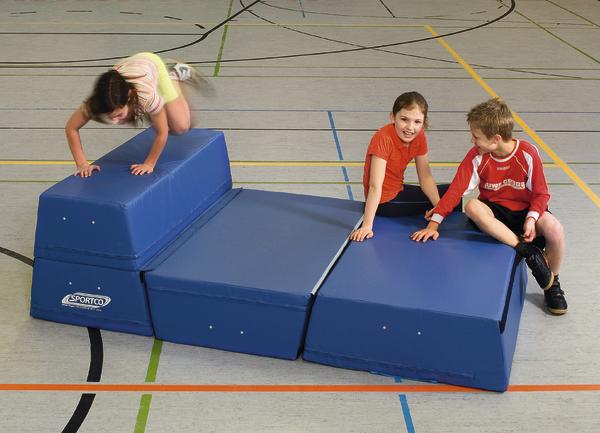 Kinder spielen und klettern auf blauen Turnmatten in einer Sporthalle.